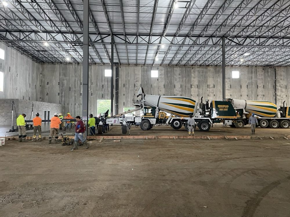 Nicolia crew placing and screeding a warehouse floor slab while two mixers discharge
